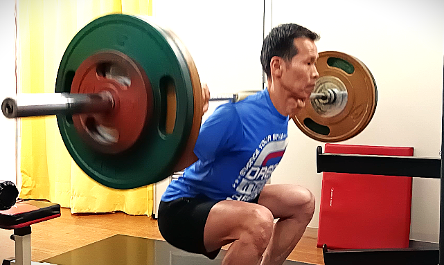 バーベルスクワットのボトムポジションで重心をコントロールするパーソナルトレーナー